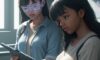 A diverse group of students in a modern classroom, where one student interacts with a glowing holographic 3D geometry shape on a tablet.