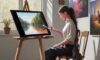 A young artist works on a physical canvas at a wooden table in a sunlit studio, with a sleek tablet displaying a vibrant AI-generated color study nearby, illustrating the blend of traditional and digital art.