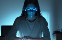 A student looks conflicted in a dimly lit room, their face illuminated by a laptop screen showing AI-generated text amidst a desk cluttered with traditional textbooks and handwritten notes.