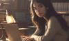 A diverse college student focused on a laptop in a sun-drenched library, surrounded by books and a mug of coffee.