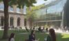 A diverse group of students sitting on a green lawn in a modern university courtyard, talking and studying near a blend of historic stone and contemporary glass architecture in soft morning sunlight.