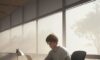 A focused college student studying calculus at a wooden desk in a sunlit, modern university library with textbooks and a laptop.
