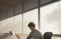 A focused college student studying calculus at a wooden desk in a sunlit, modern university library with textbooks and a laptop.