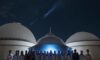 A group of diverse Indian students holding certificates and wearing badges, standing proudly in front of a large observatory dome under a starry night sky.